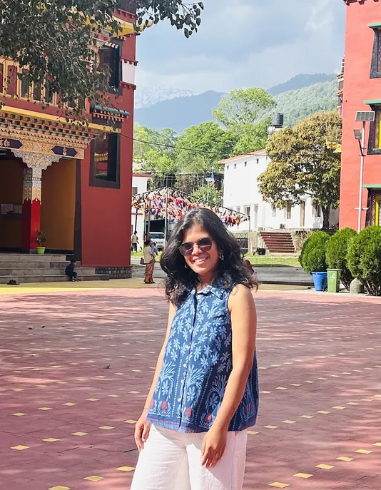 Rujuta outside a Tibetan monastery, mountains behind her